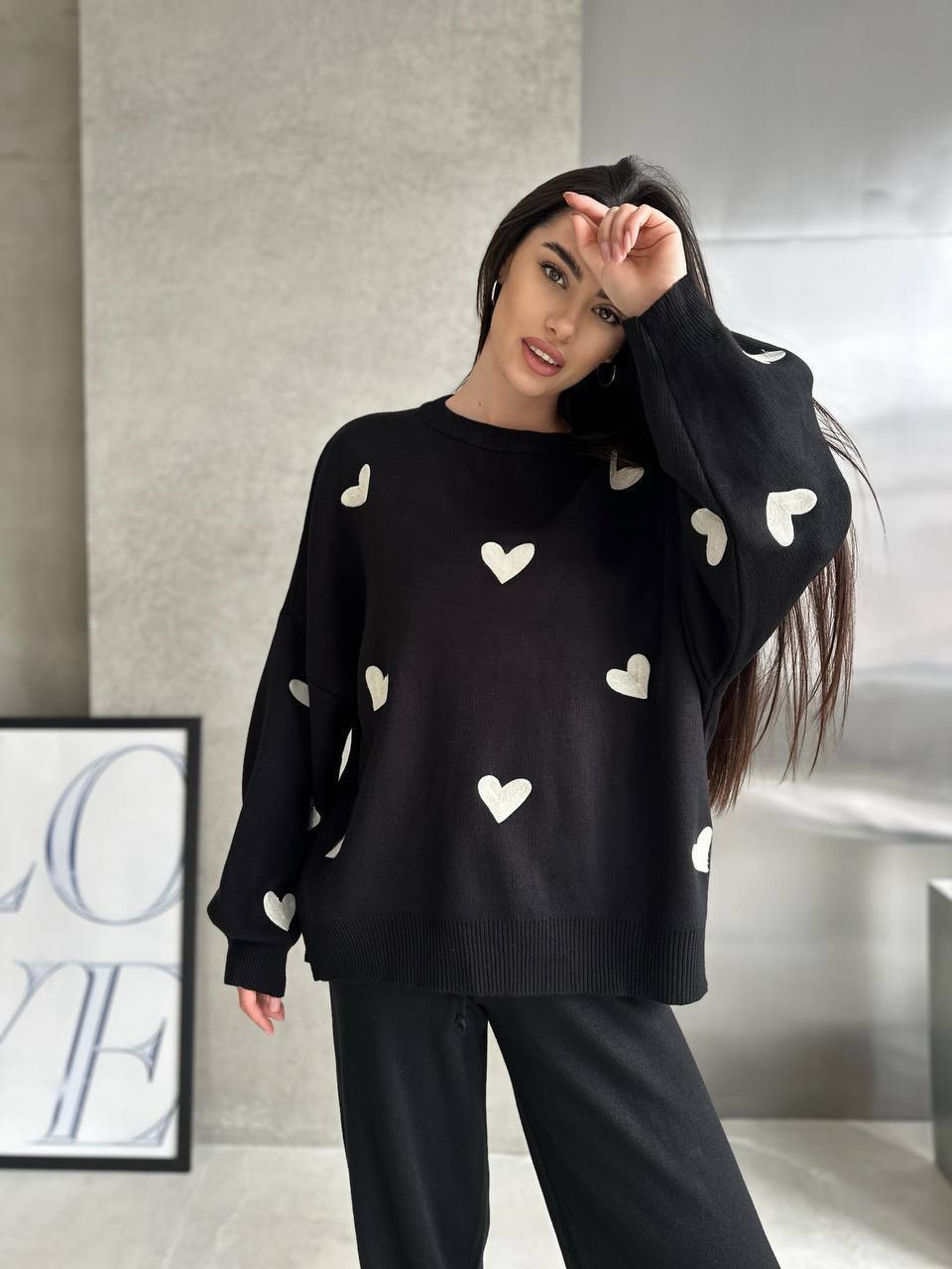 Woman wearing a black sweater with white heart patterns in a room.