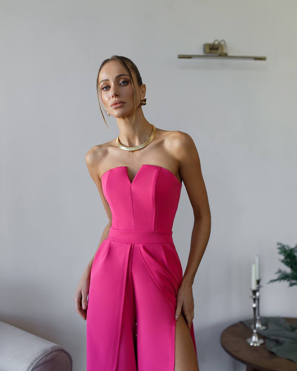 Woman wearing a bright pink strapless dress with a slit, standing indoors.
