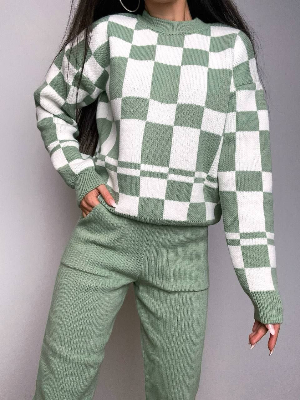 Person wearing a green and white checkered sweater and pants against a plain background