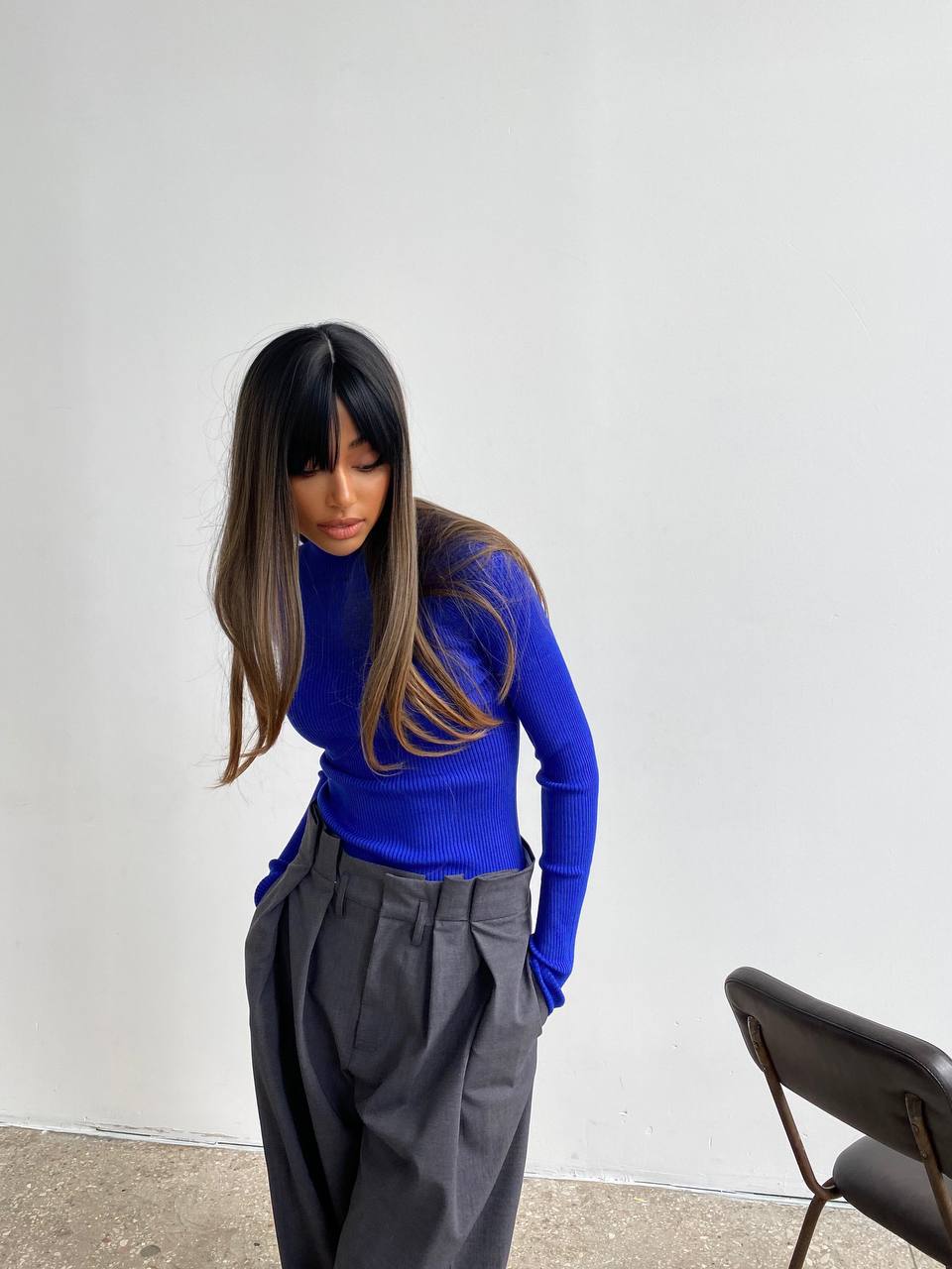 Person wearing a blue sweater and gray pants against a white wall.