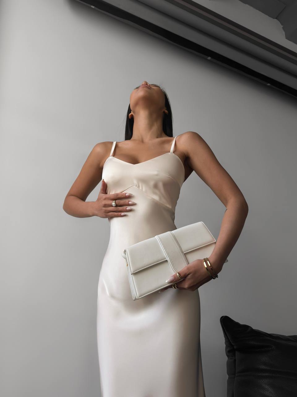 Woman in a white dress holding a clutch against a plain background