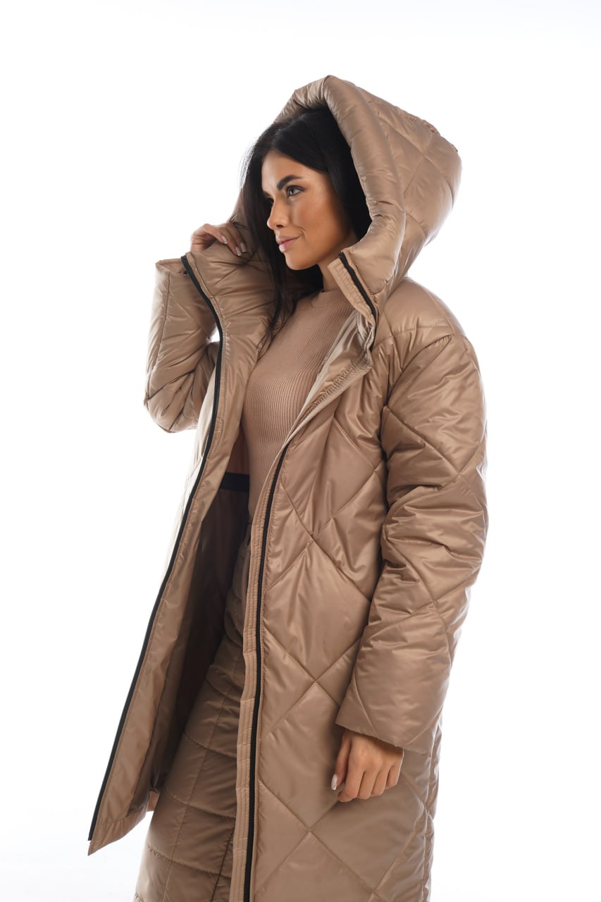 Woman wearing a long beige quilted coat with a hood on a white background