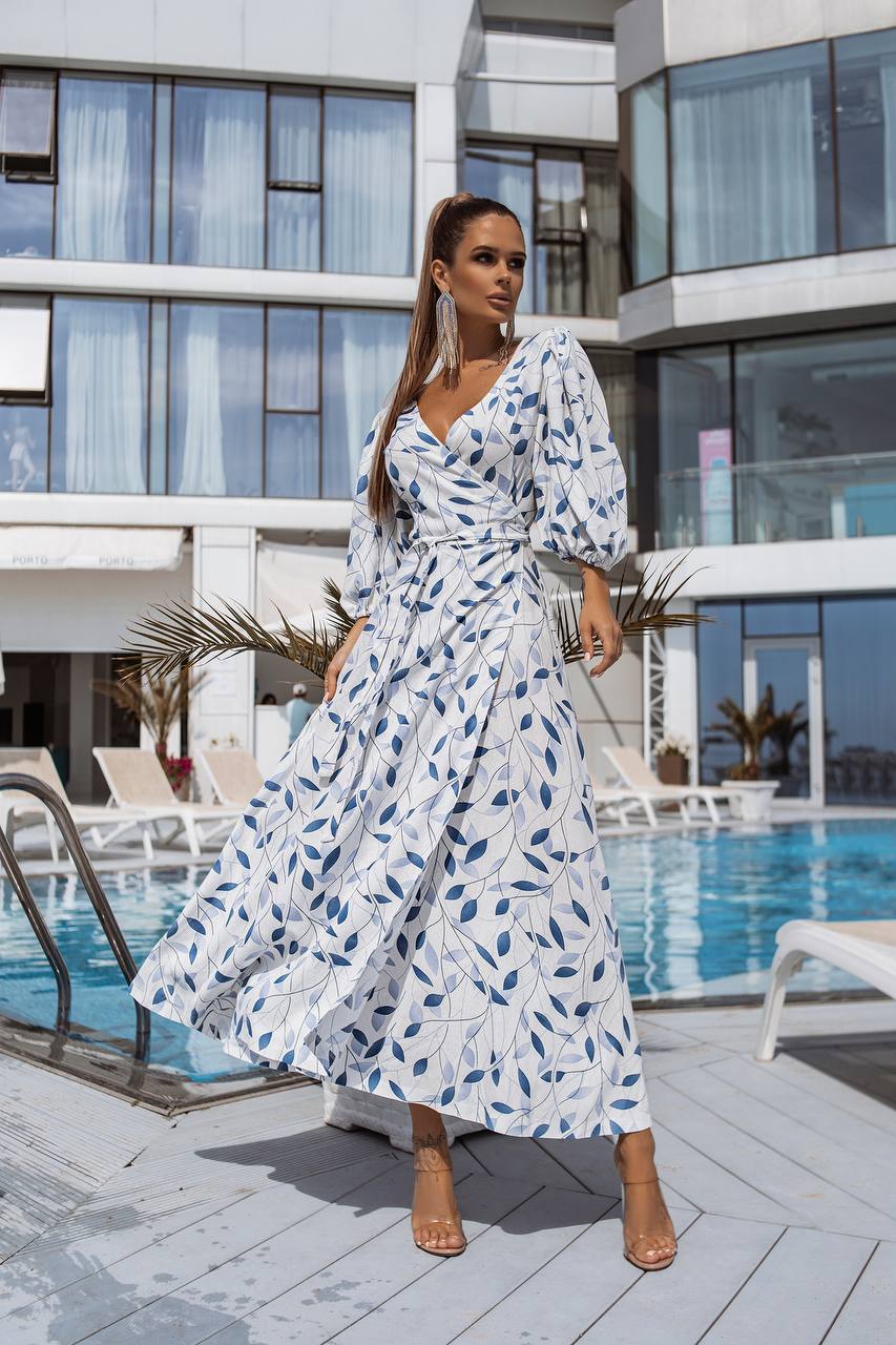 Woman in a white dress with blue leaf pattern standing by a poolside.
