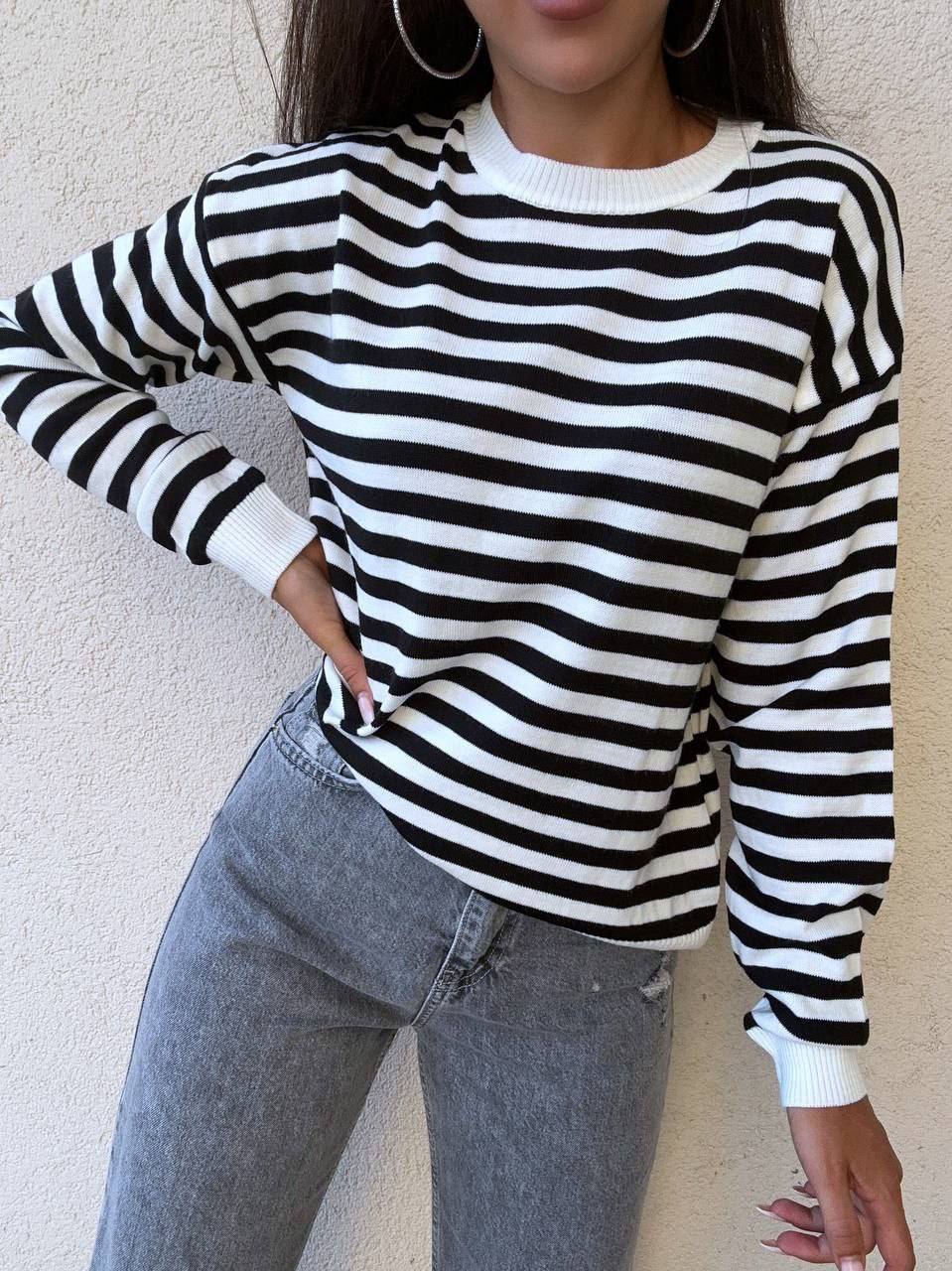 Person wearing a black and white striped sweater and light blue jeans against a neutral background