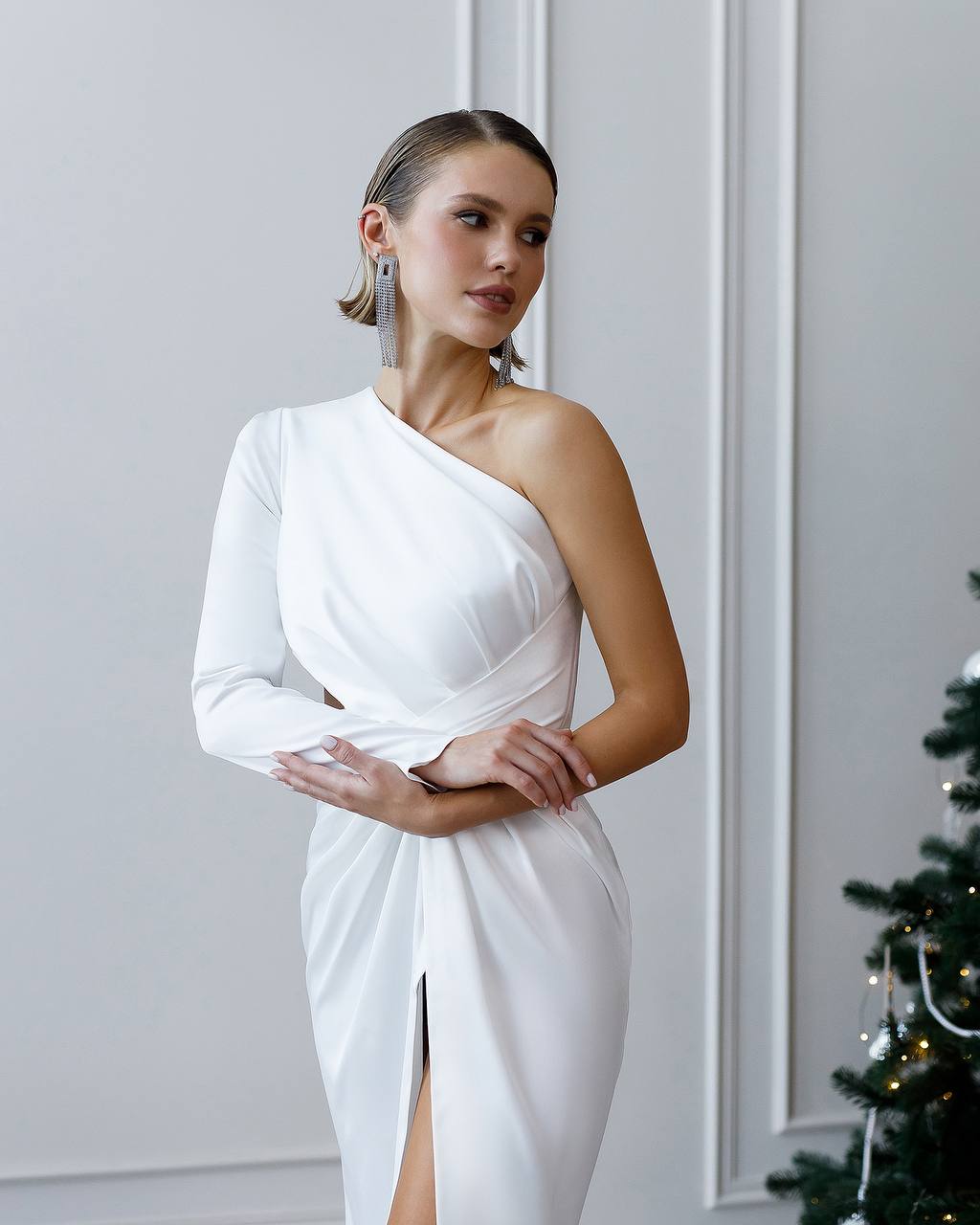 Woman wearing a white one-shoulder dress with a Christmas tree in the background