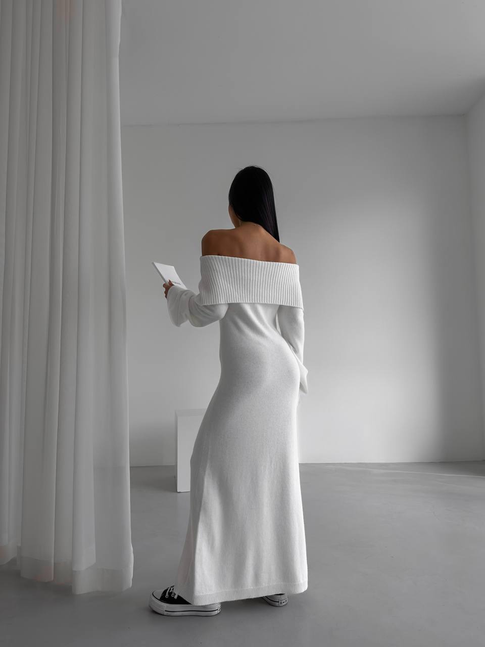 Woman in a white off-shoulder dress standing in a minimalistic room.