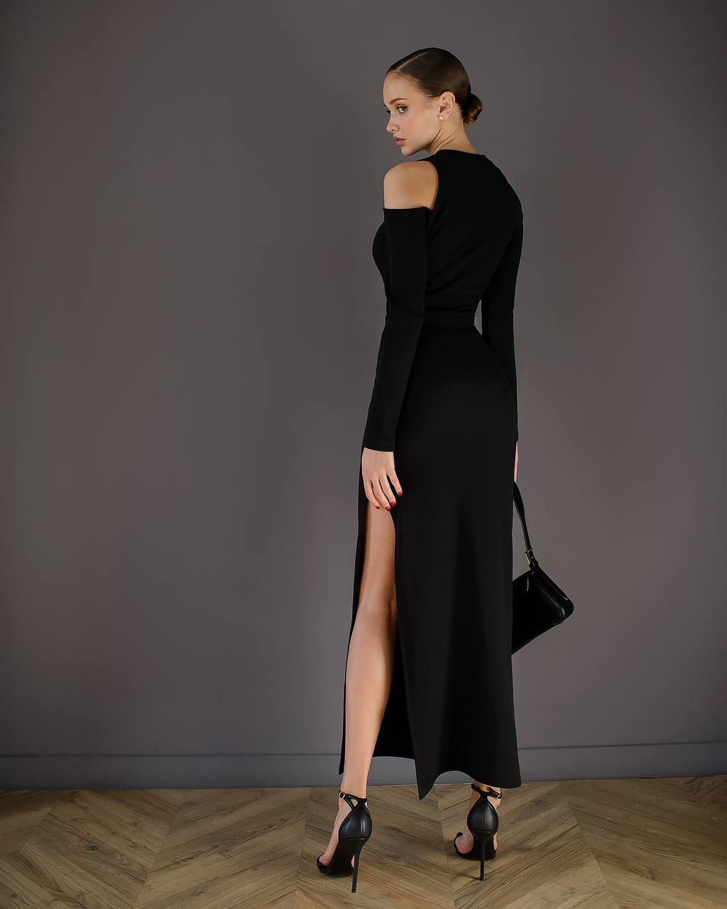 Woman wearing a black dress with a high slit, standing against a plain background.