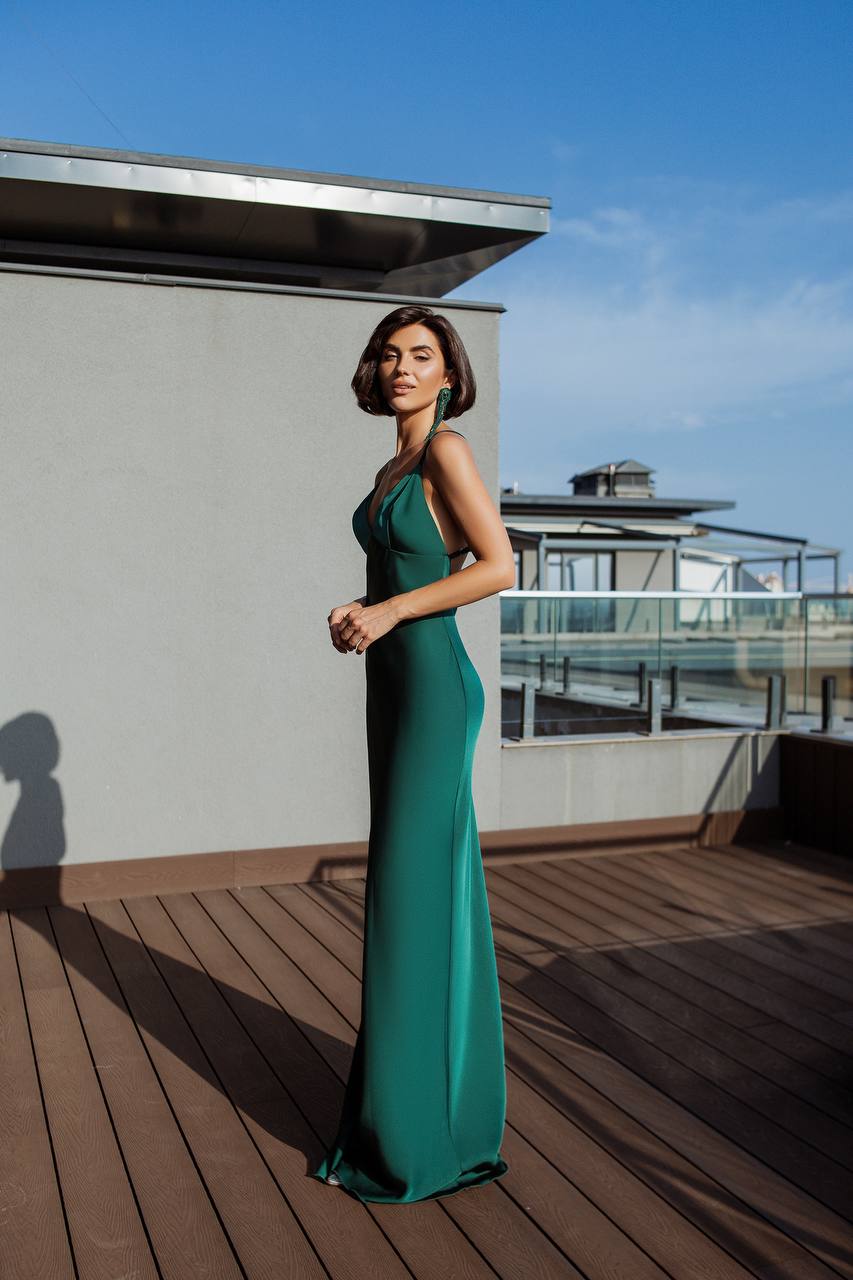 Woman in a green evening gown standing on a rooftop with a clear blue sky.