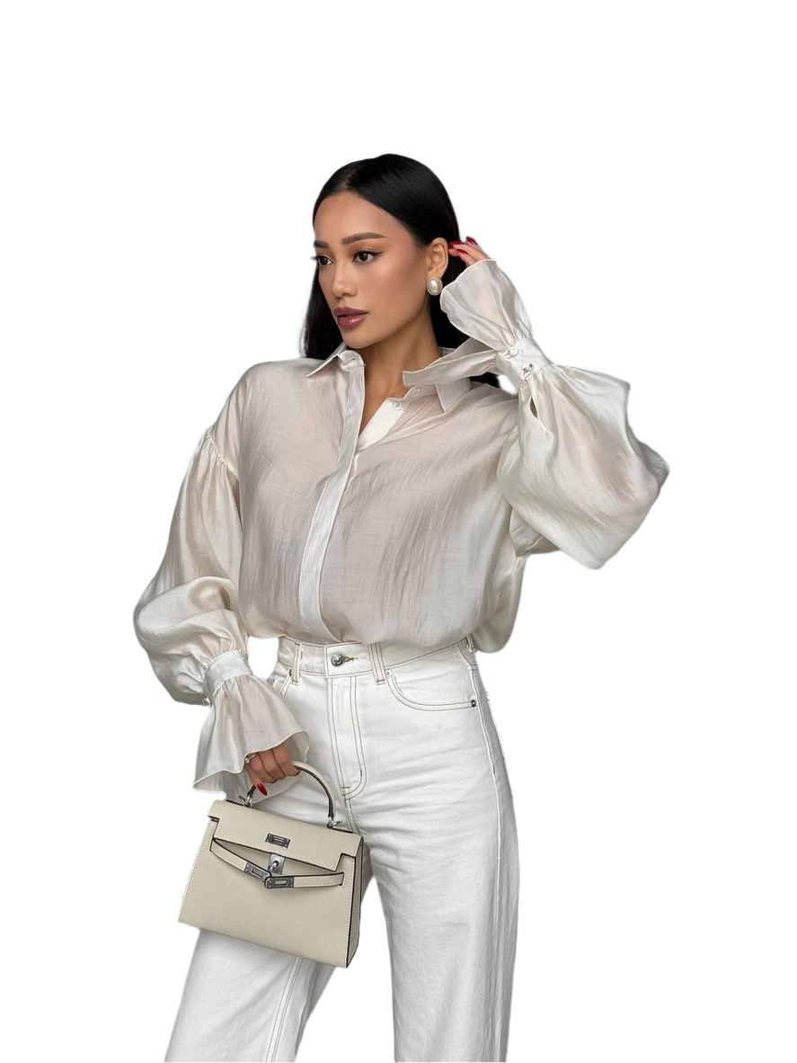 Woman wearing a sheer white blouse and white pants, holding a beige handbag on a white background