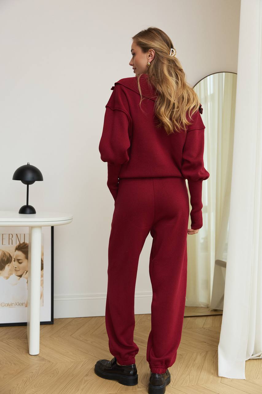 Woman in a red outfit standing in a room with a mirror and table.