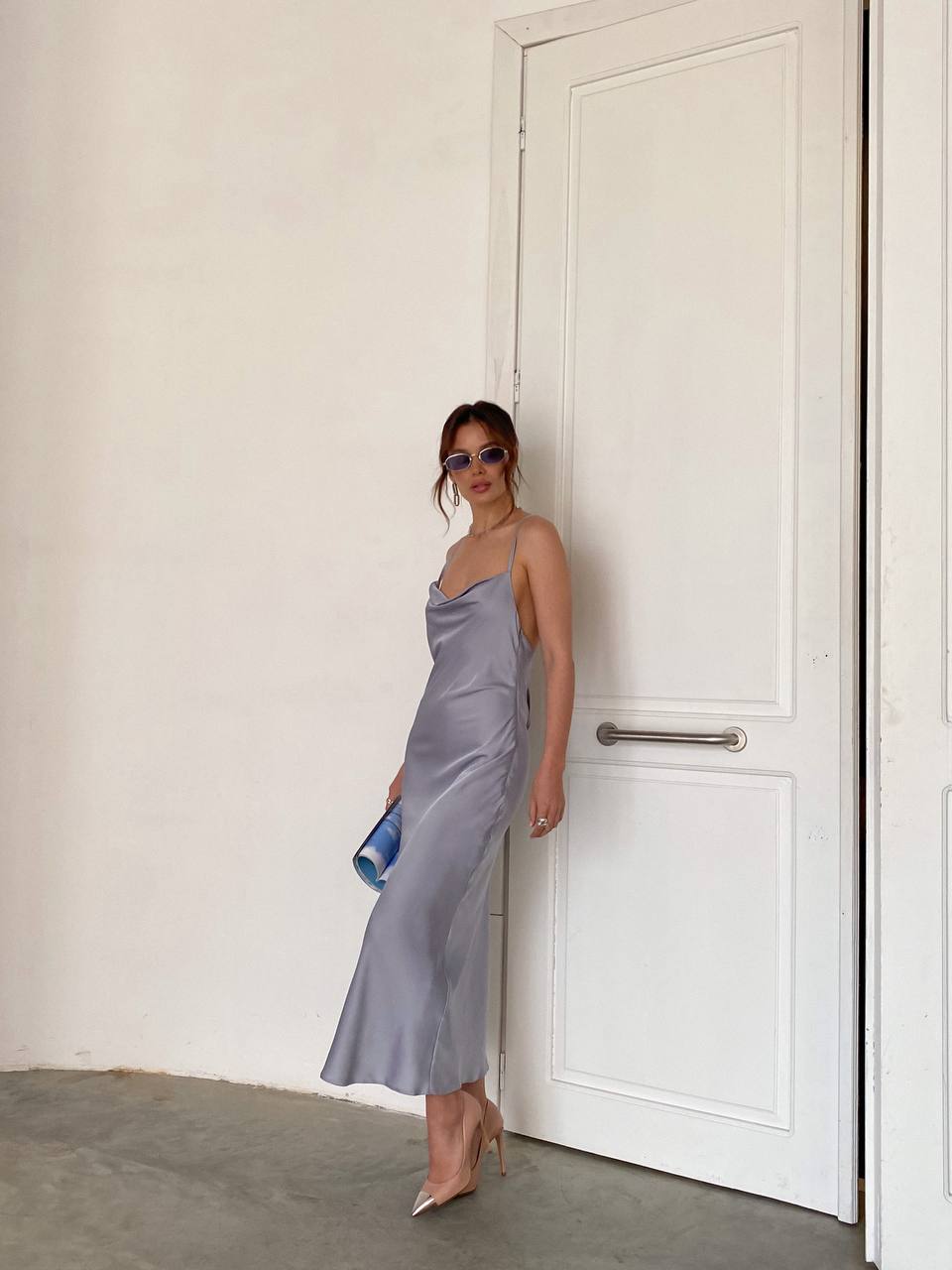 Woman in a light gray dress standing against a white door.