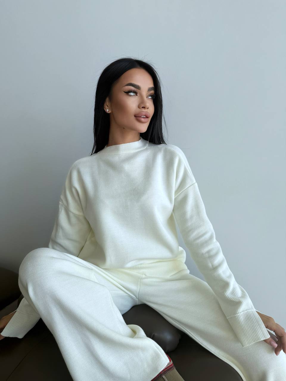 Woman wearing a white outfit sitting against a plain background