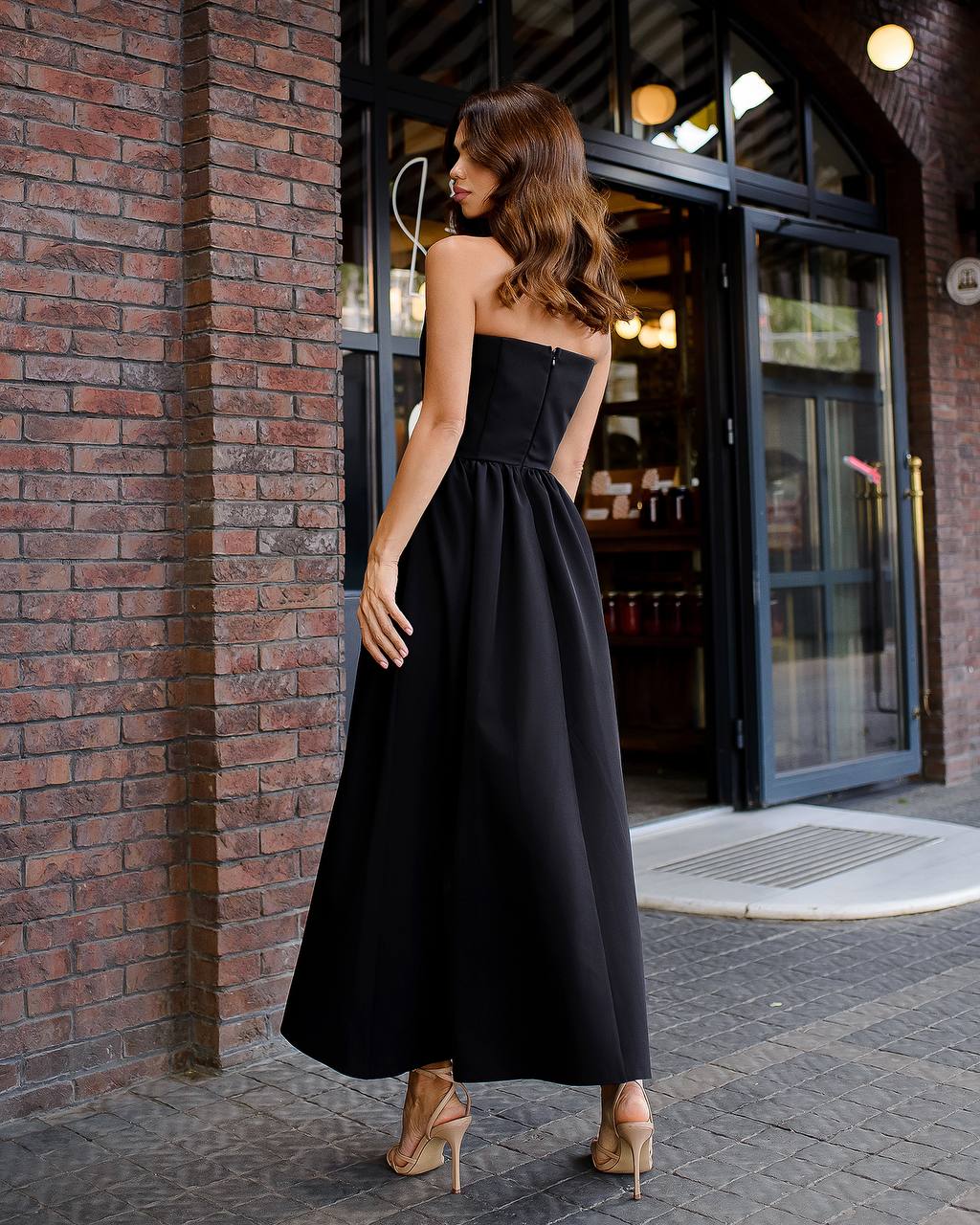 Woman in a black strapless dress standing against a brick wall.