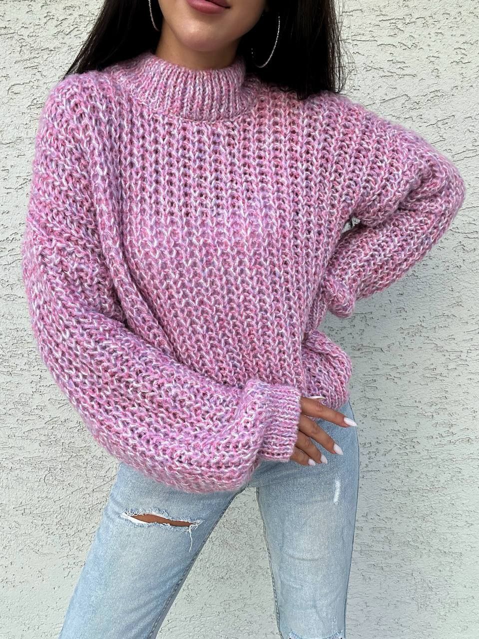 Person wearing a pink knitted sweater and light blue jeans against a neutral background
