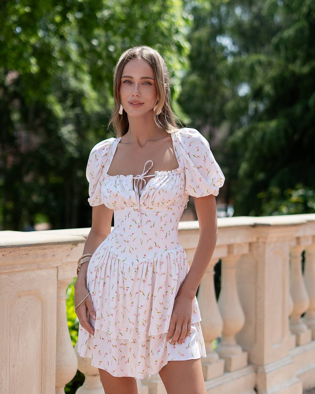 Woman in a white floral dress standing outdoors with greenery in the background