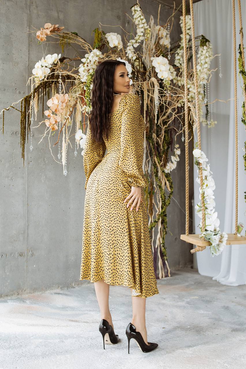 Woman in a gold dress standing in front of floral decorations.