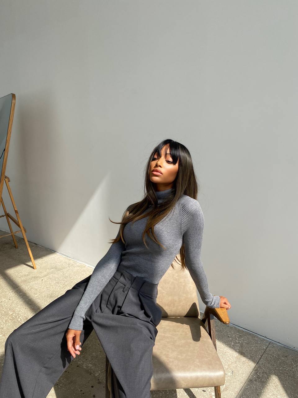 Woman in a gray outfit sitting on a chair with a minimal background