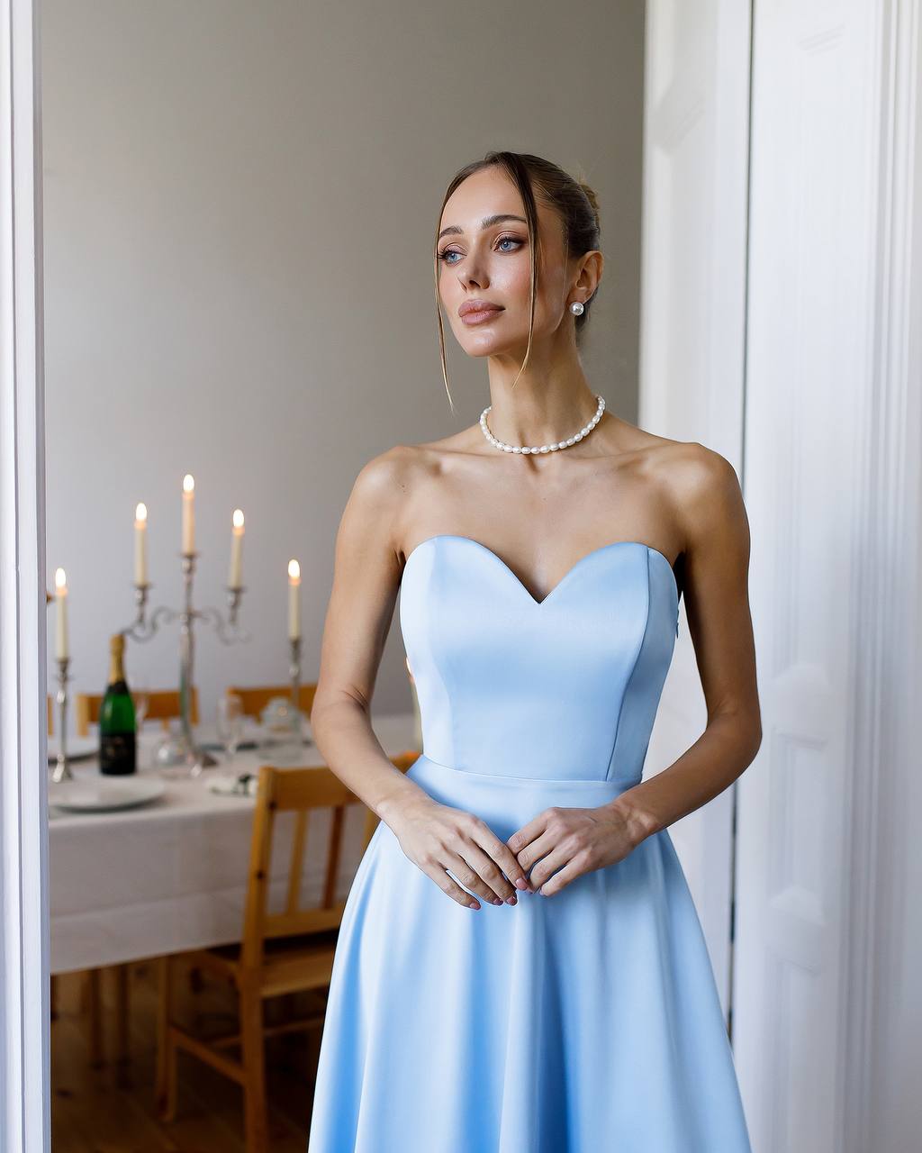 Woman in a light blue dress standing in a room with a dining table in the background