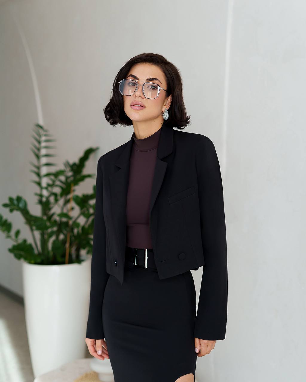 Woman wearing a black blazer and skirt set with a plant in the background