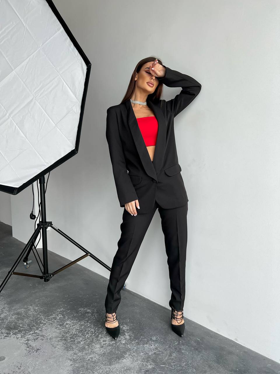 Woman in a black suit with a red top posing in a studio setting.