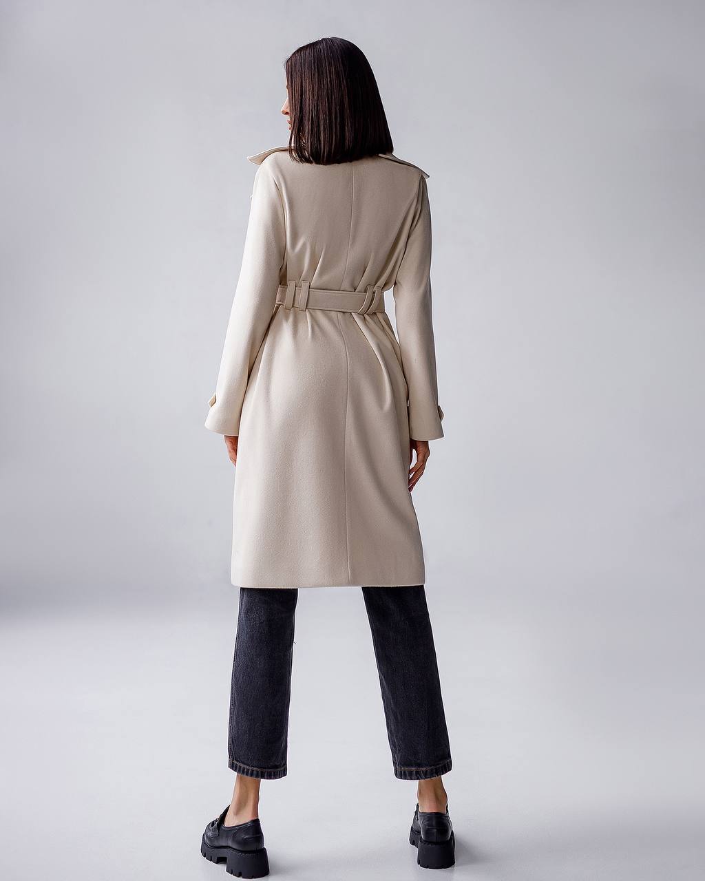 Woman wearing a beige trench coat on a plain background