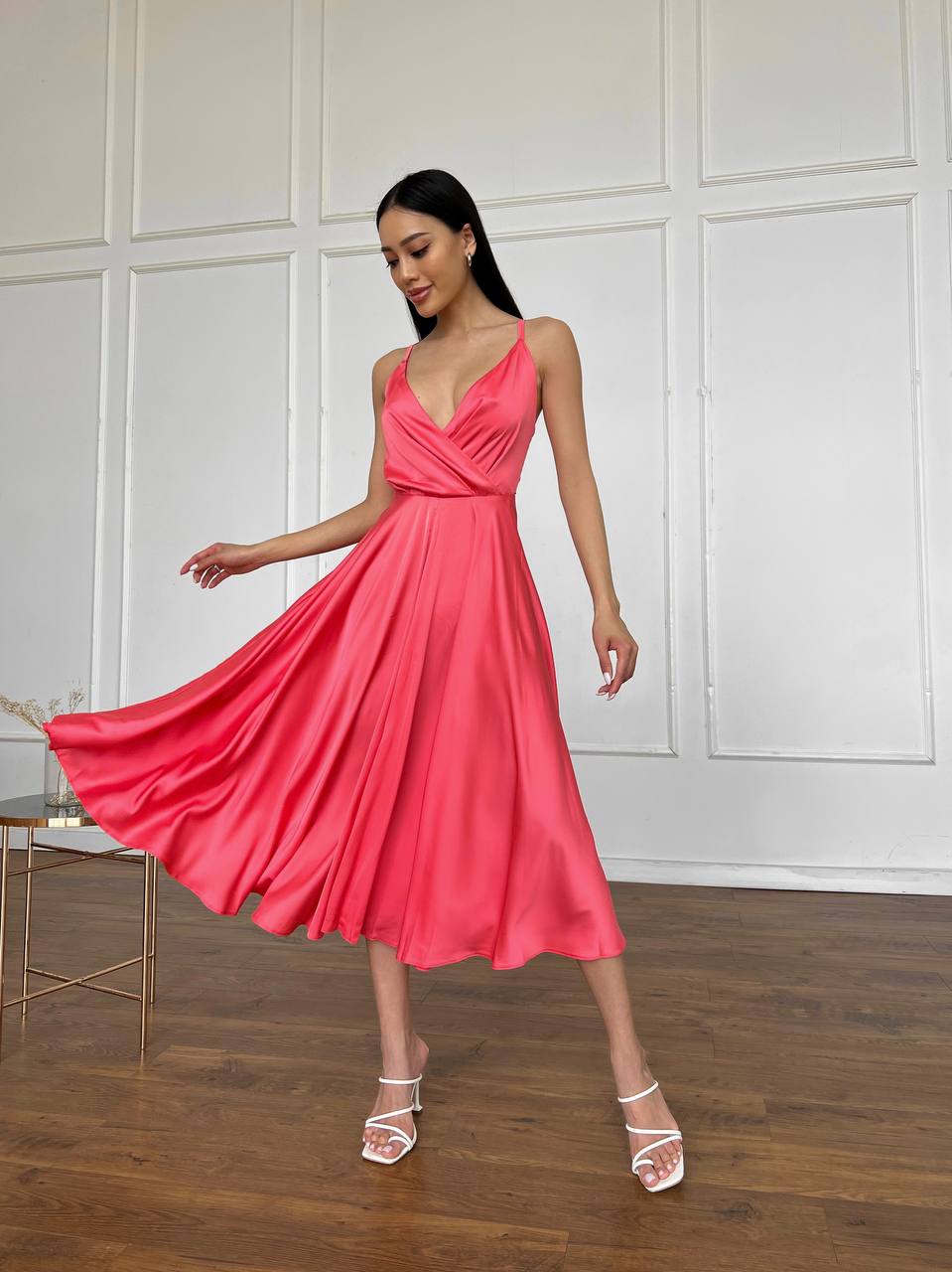 Woman in a pink dress standing in a room with wooden floor and white paneled walls.