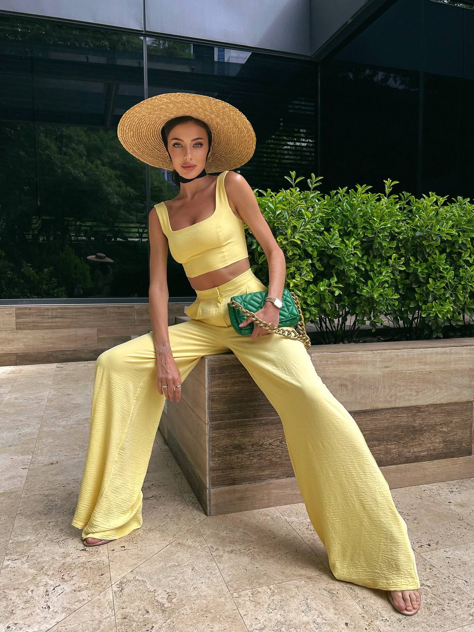 Woman in a yellow outfit with a wide-brimmed hat sitting on a bench outdoors.