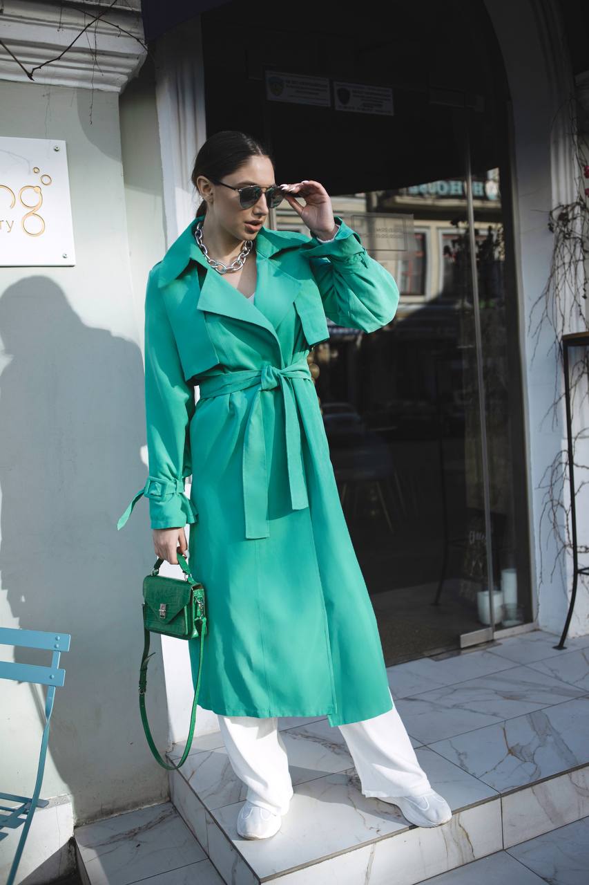 Woman in a green trench coat standing outside a building