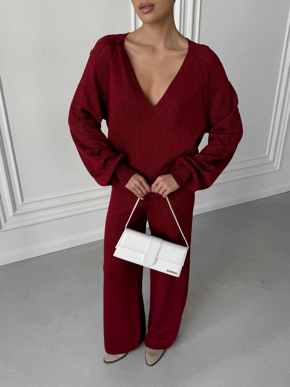Person wearing a burgundy outfit holding a white handbag against a neutral background