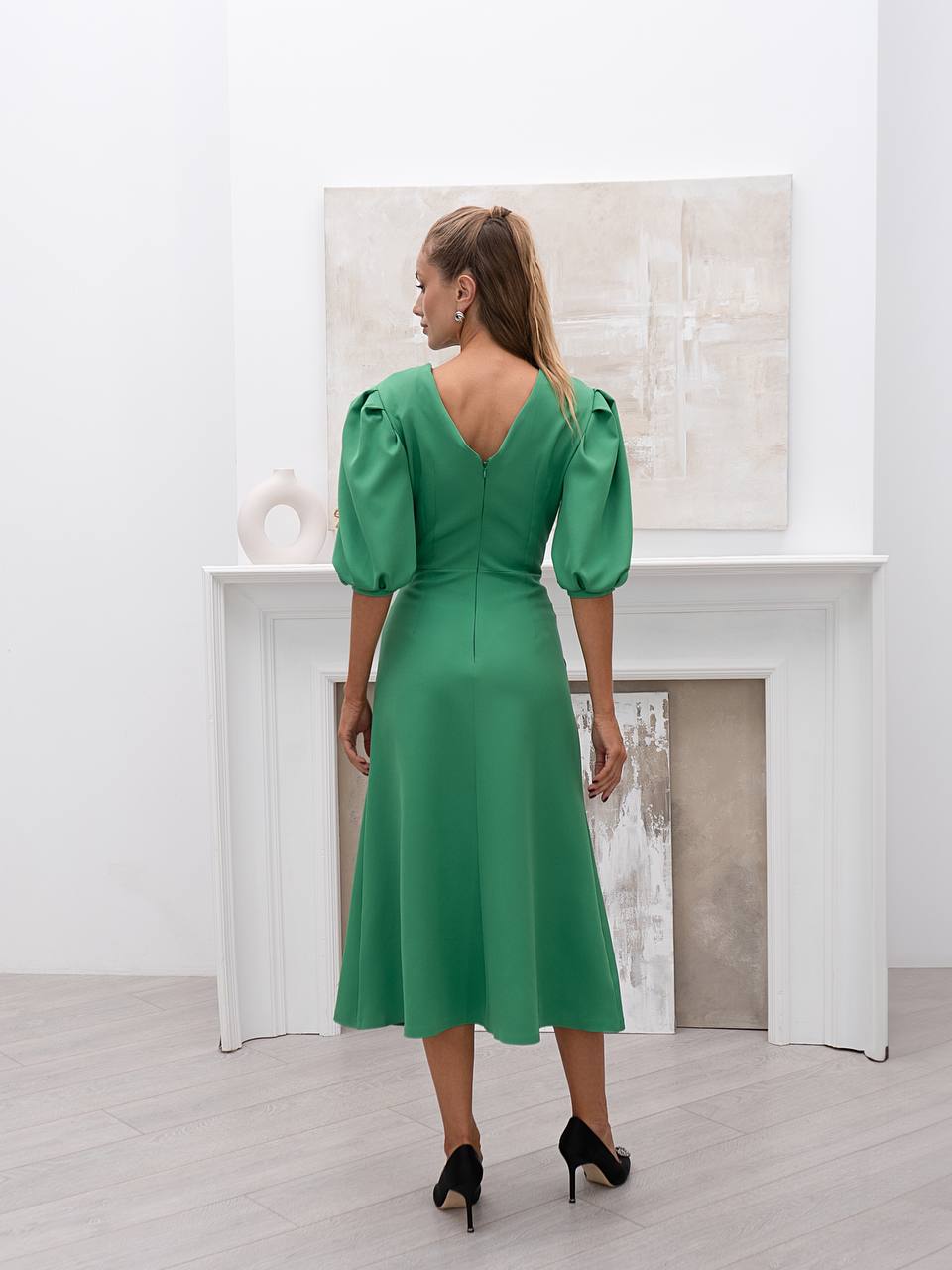 Woman in a green dress standing in a room with a white fireplace.