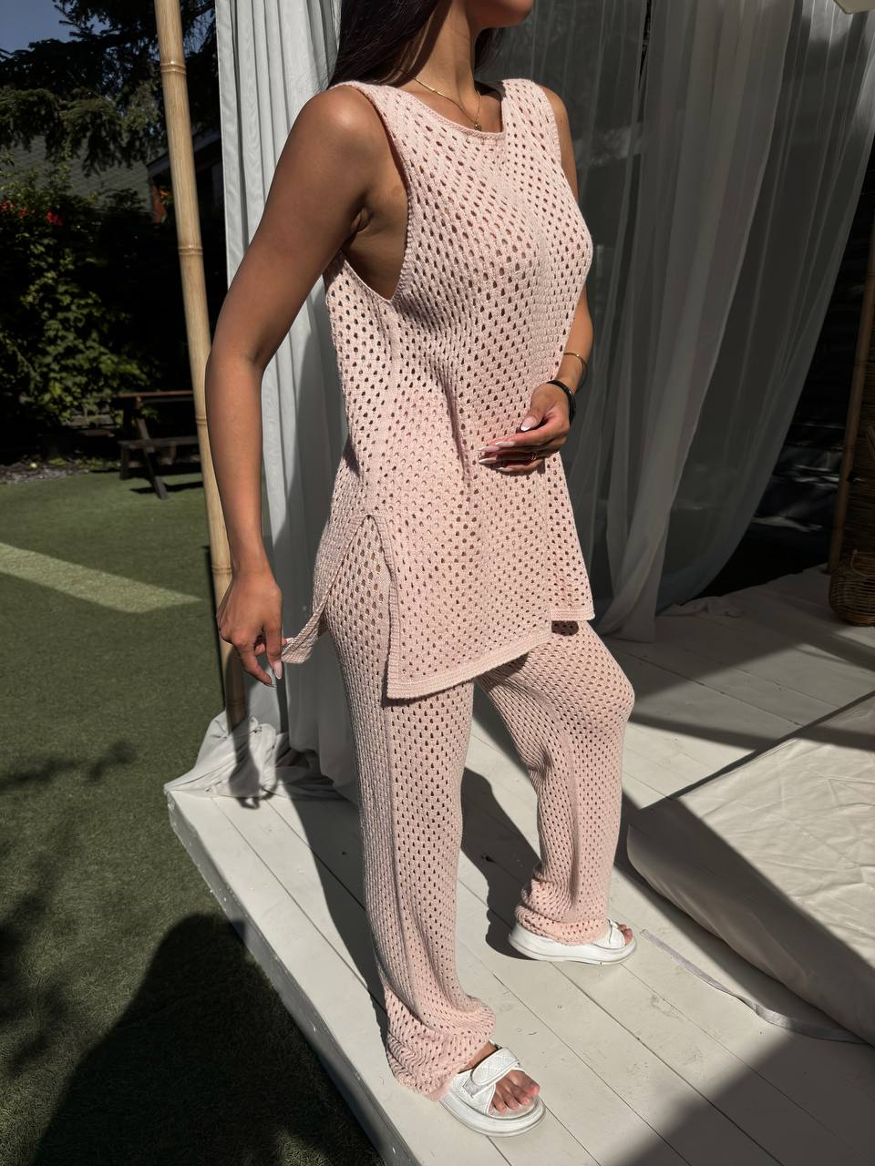 Person wearing a pink crochet outfit standing on a wooden deck.