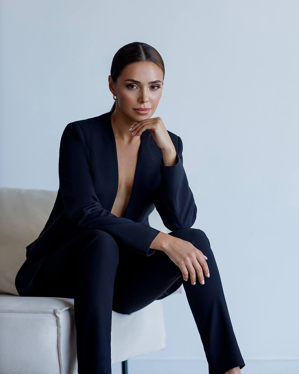 Woman in a black suit sitting on a white chair against a light gray background