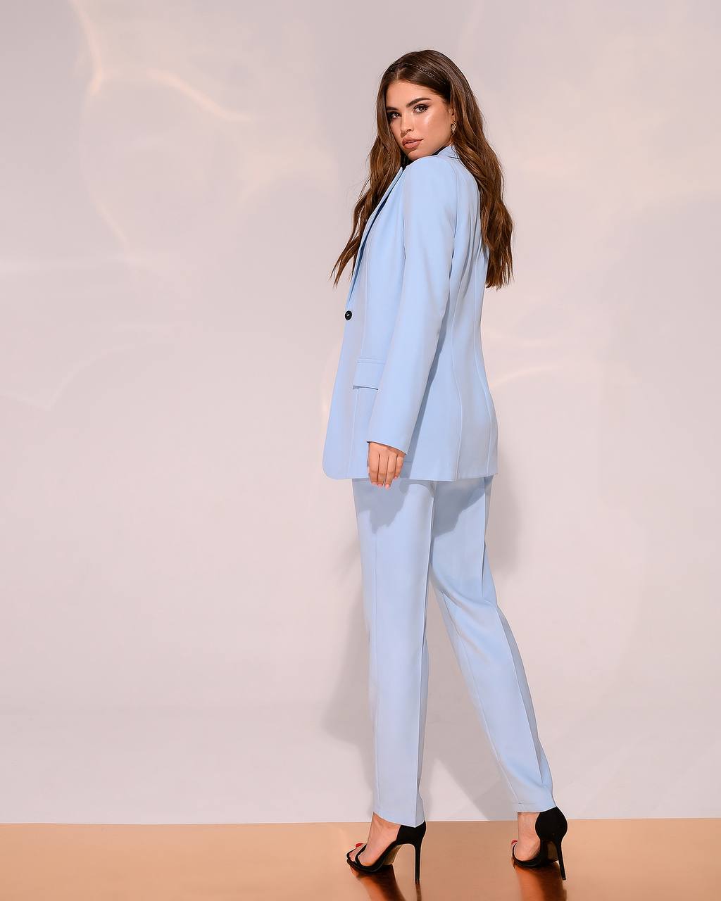 Woman wearing a light blue suit standing against a plain background