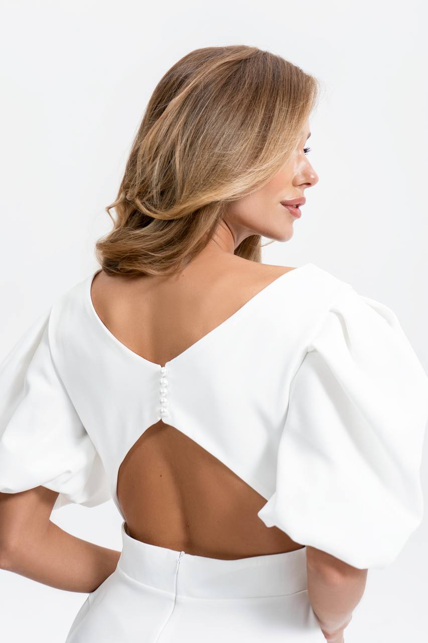 Woman wearing a white dress with a cutout design on a plain background