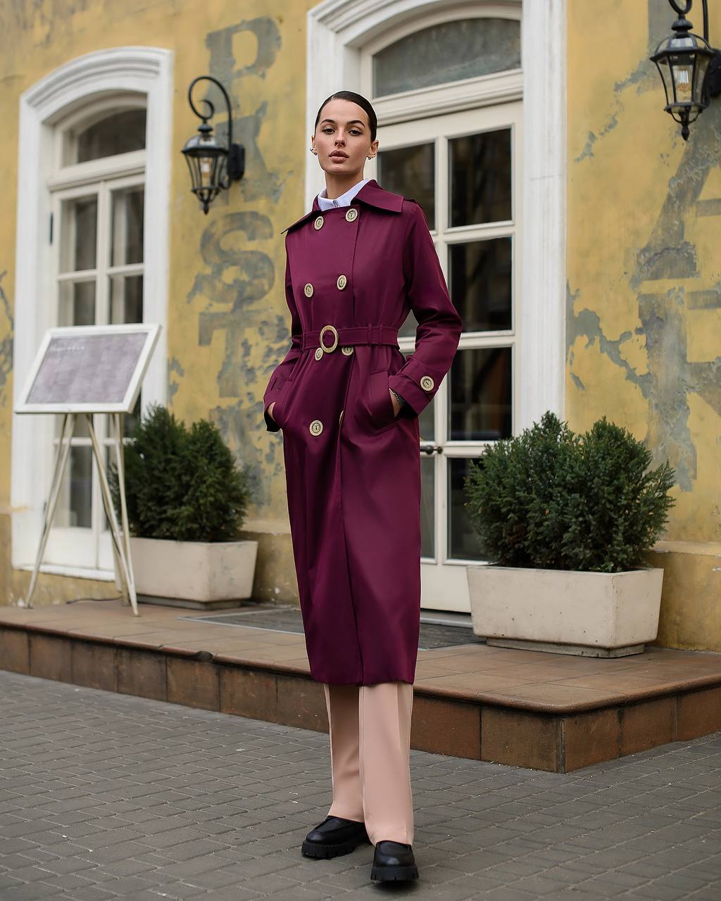 Woman in a purple coat standing in front of a building with decorative elements.