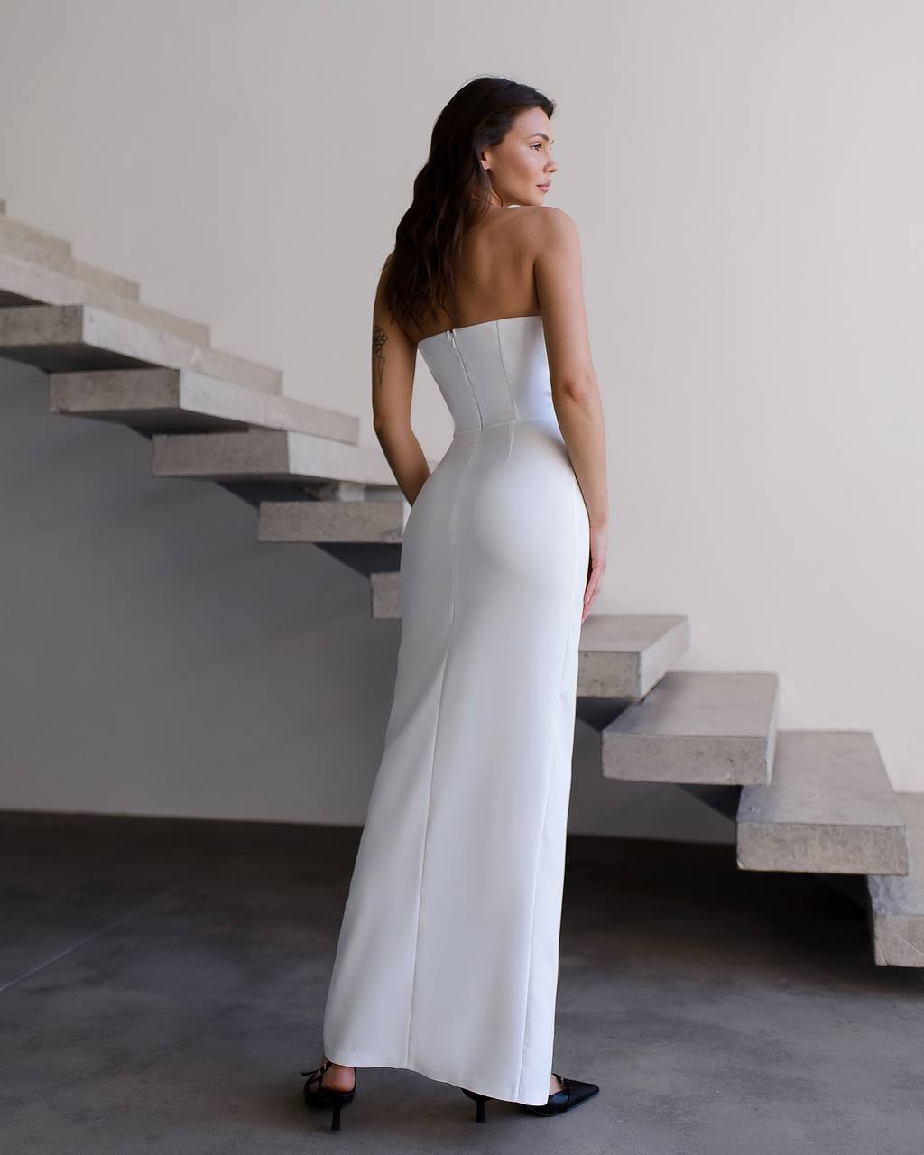 Woman in a strapless white gown standing in front of concrete stairs.