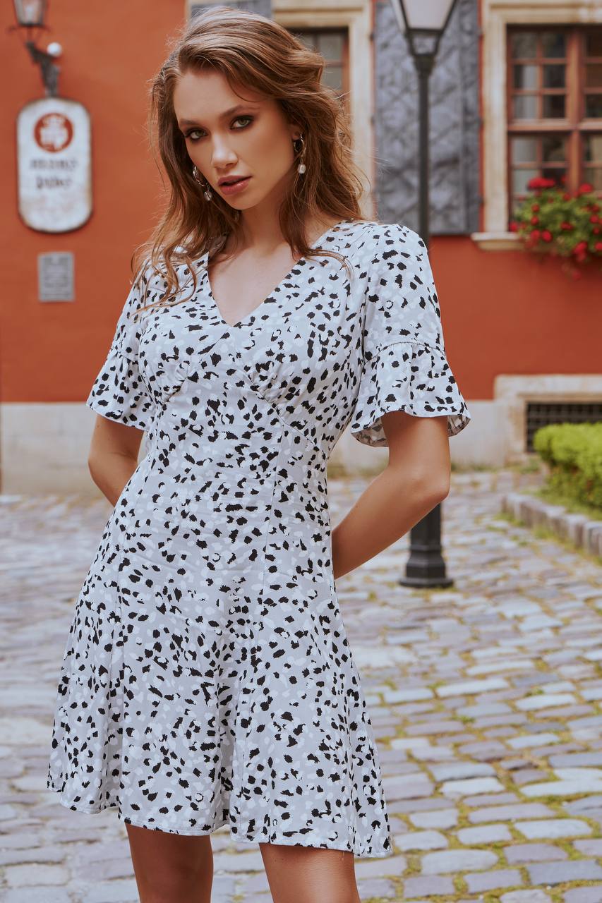 Woman wearing a white dress with black polka dots on a cobblestone street.