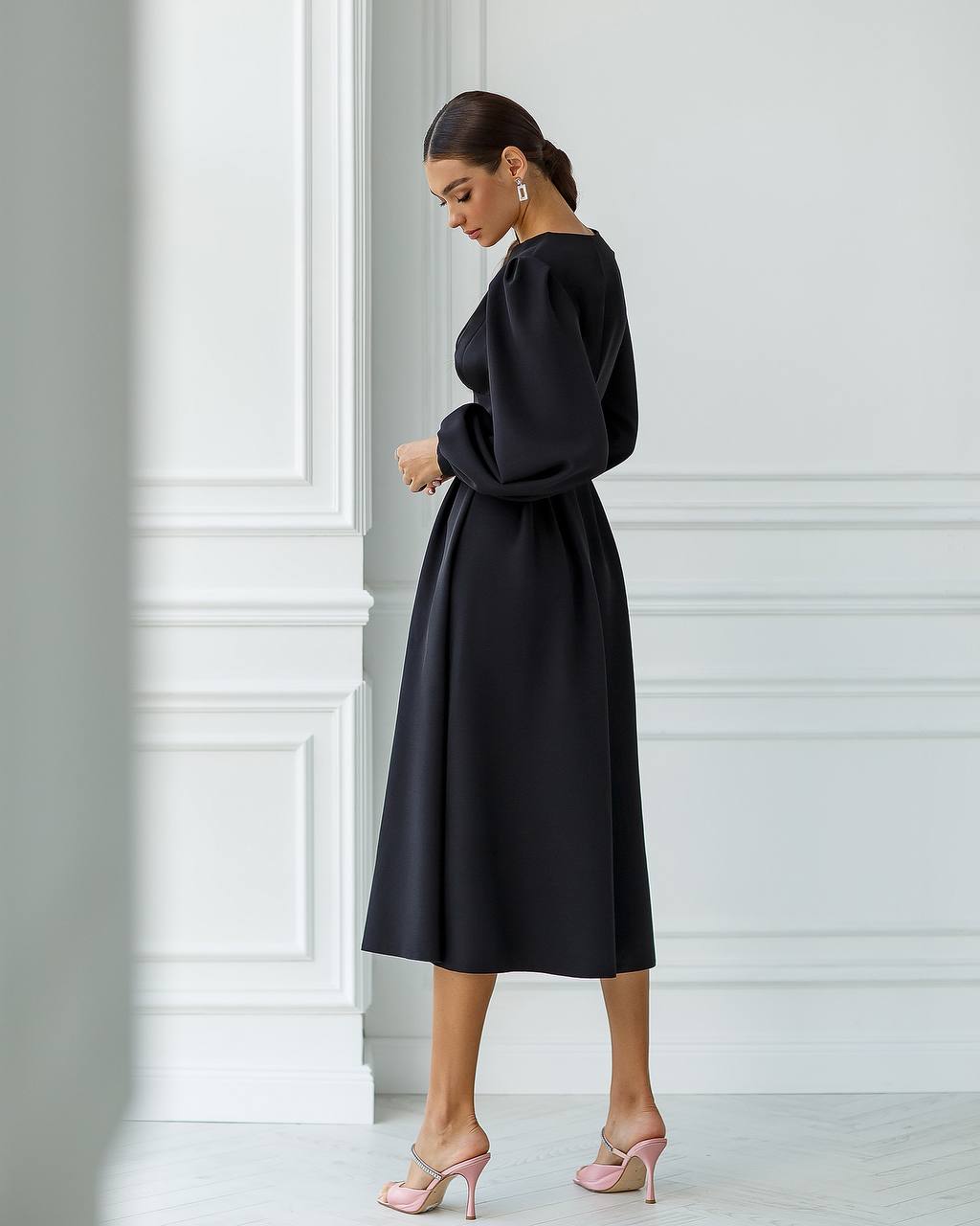 Woman wearing a black dress standing against a white wall.