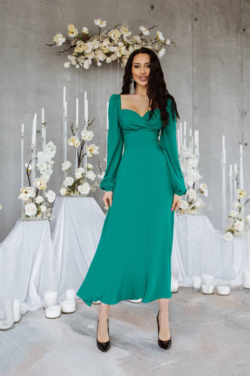 Woman in a green dress standing in front of floral arrangements and candles.