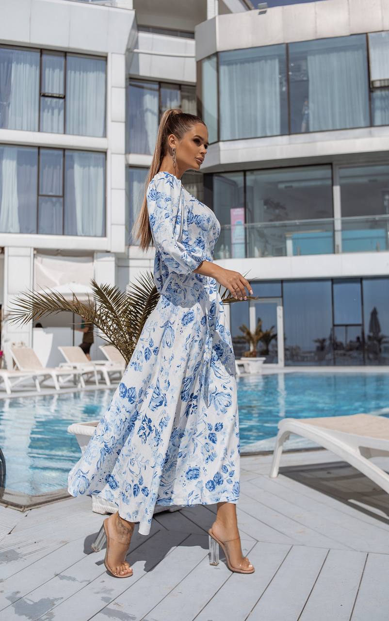 Woman in a blue floral dress standing by a poolside with modern building in the background