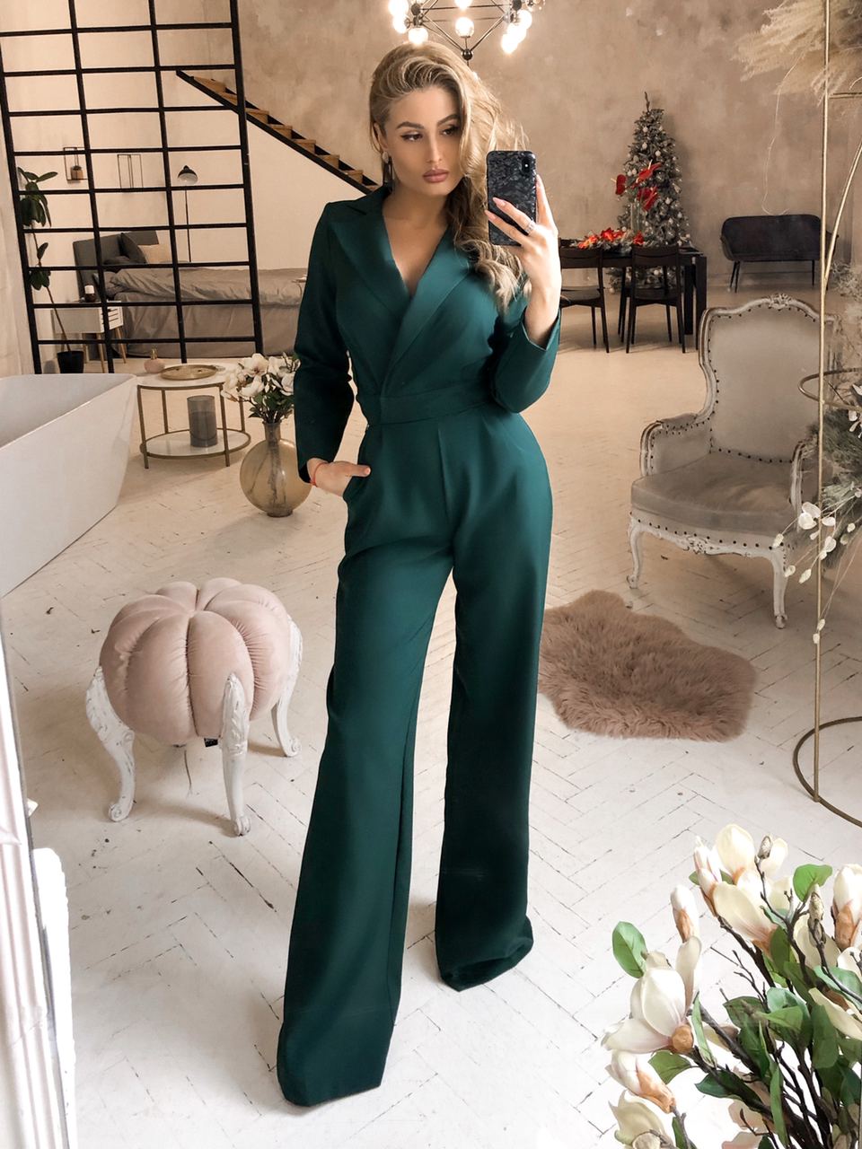 Woman taking a mirror selfie wearing a green jumpsuit in a stylish room.