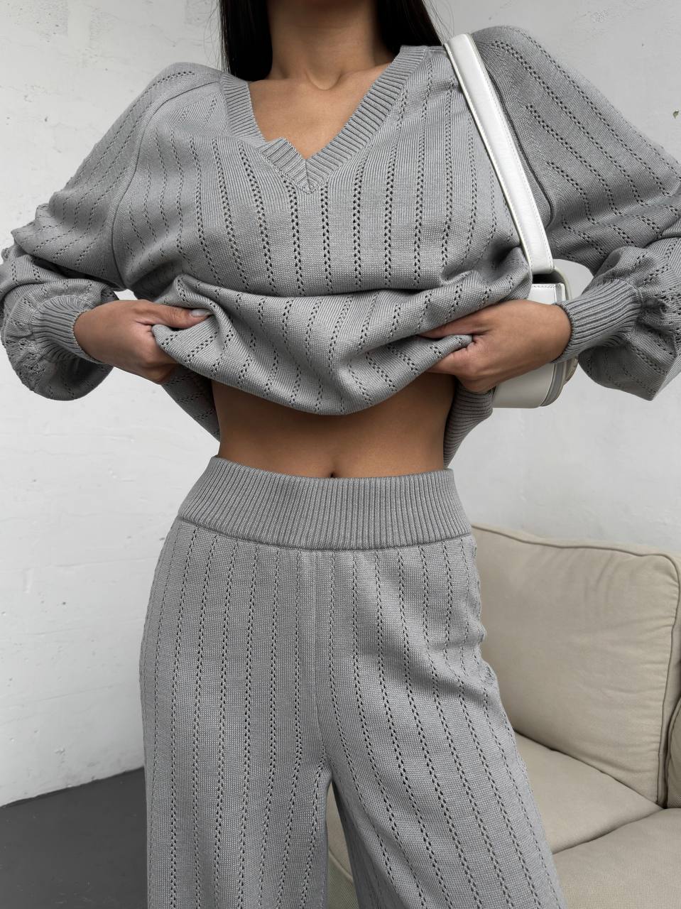 Person wearing a gray knit outfit with a white bag against a neutral background
