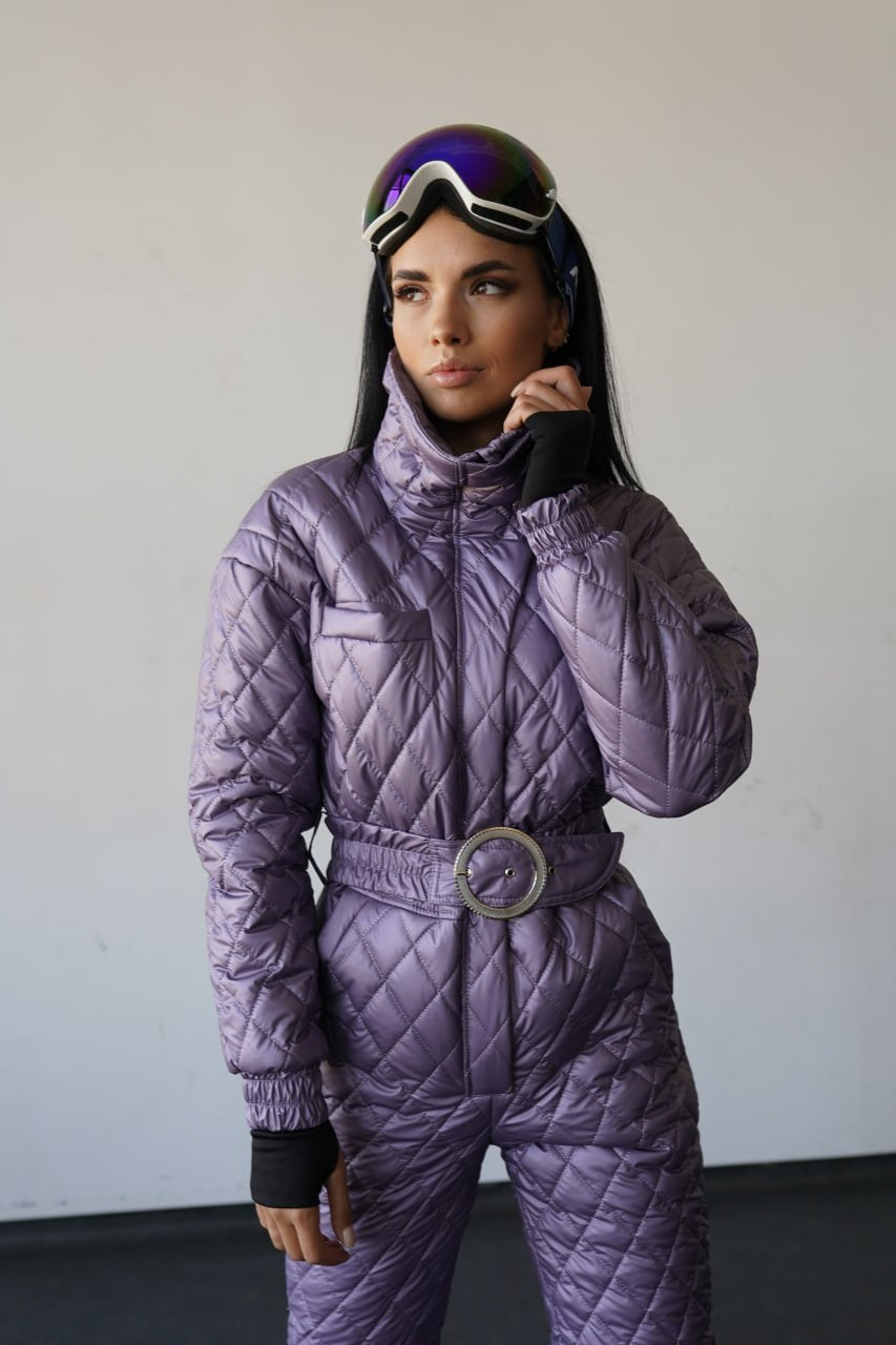Person wearing a purple quilted snowsuit with goggles on a plain background