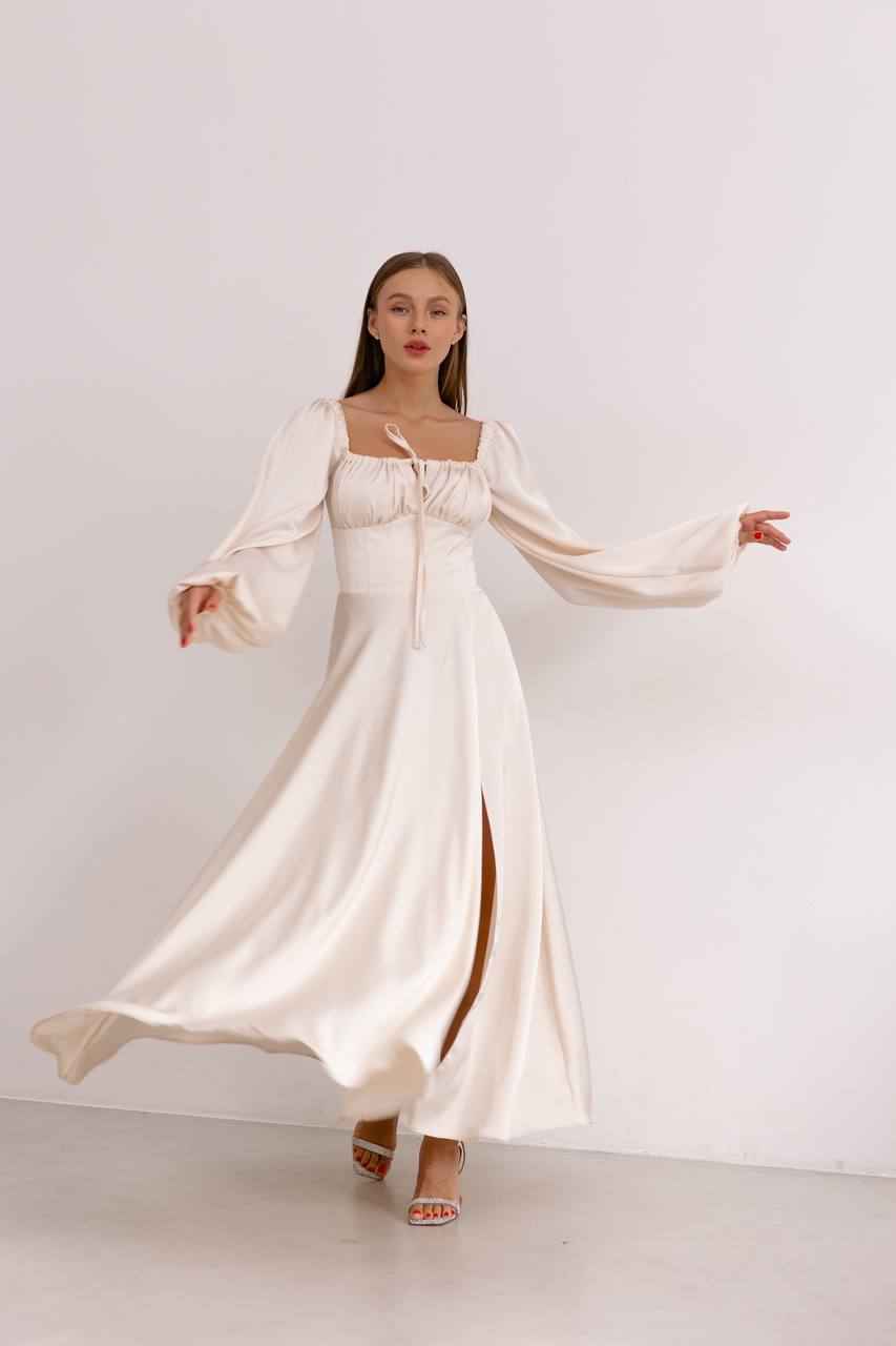 Woman wearing a long, flowing white dress with wide sleeves against a plain background