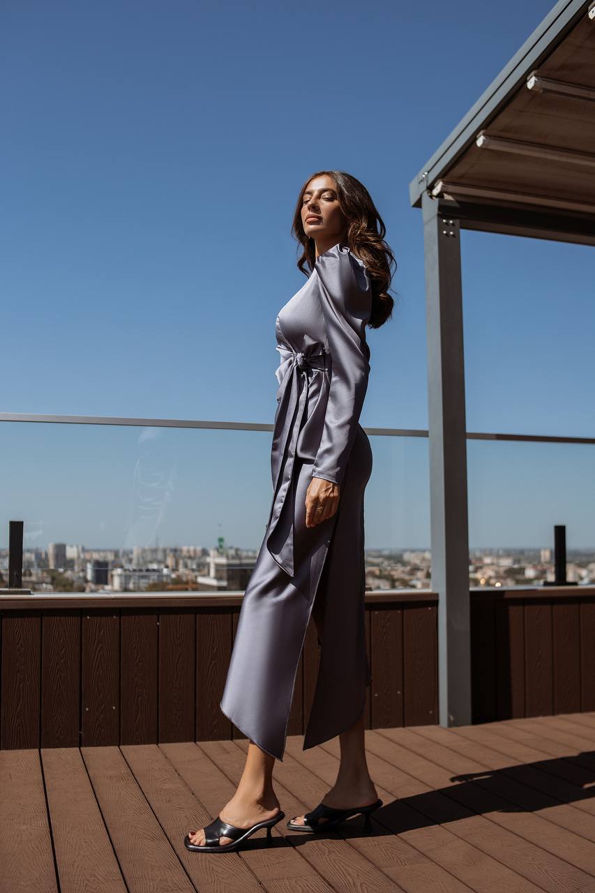 Woman in a gray outfit standing on a rooftop deck with a cityscape view.