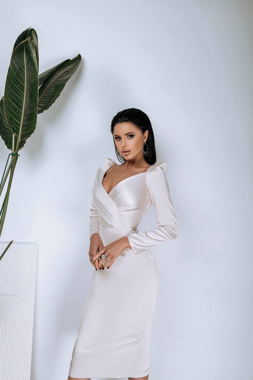 Woman in a white dress standing next to a plant against a light gray background