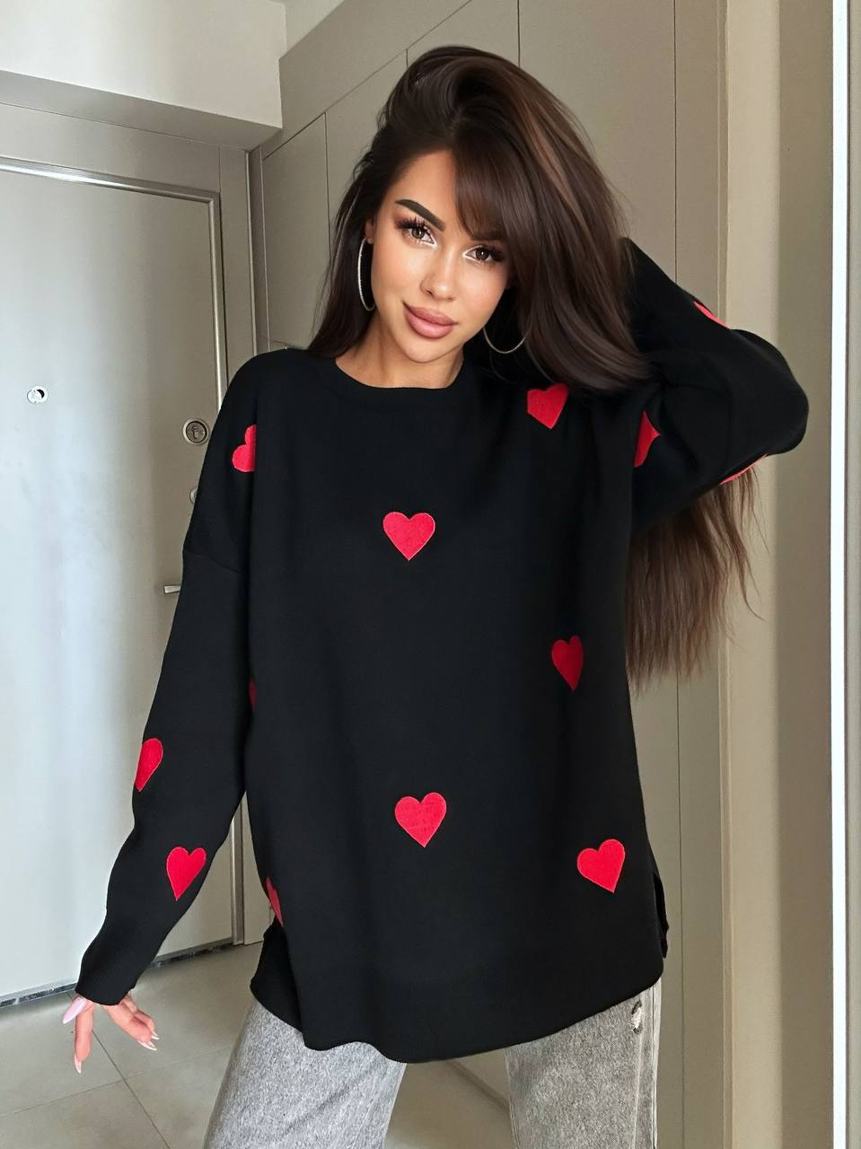 Woman wearing a black sweater with red heart patterns indoors.