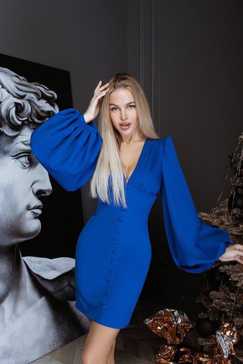Woman in a blue dress posing in front of classical sculpture and decorative elements.