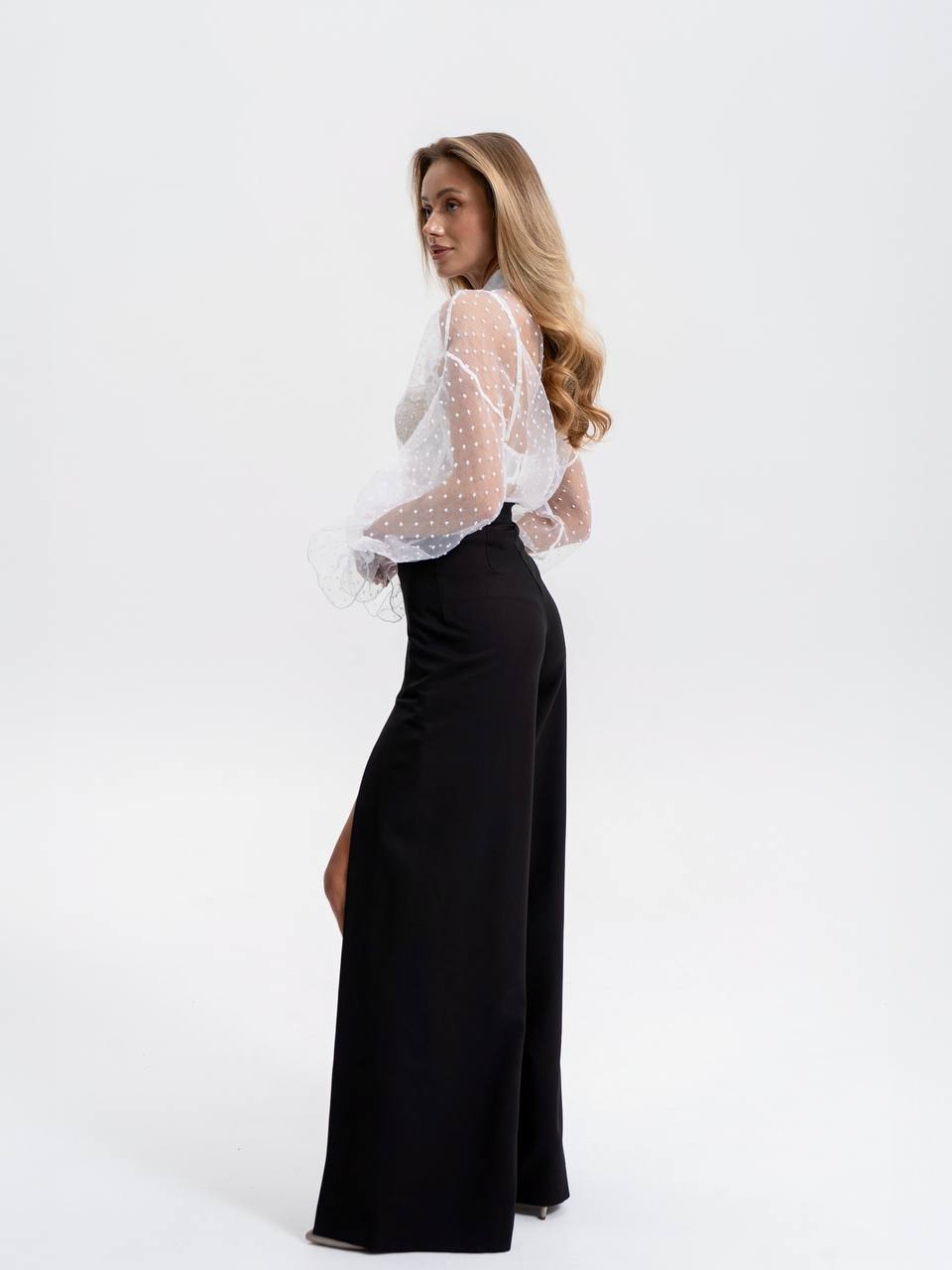 Woman wearing a white sheer top and black pants on a white background