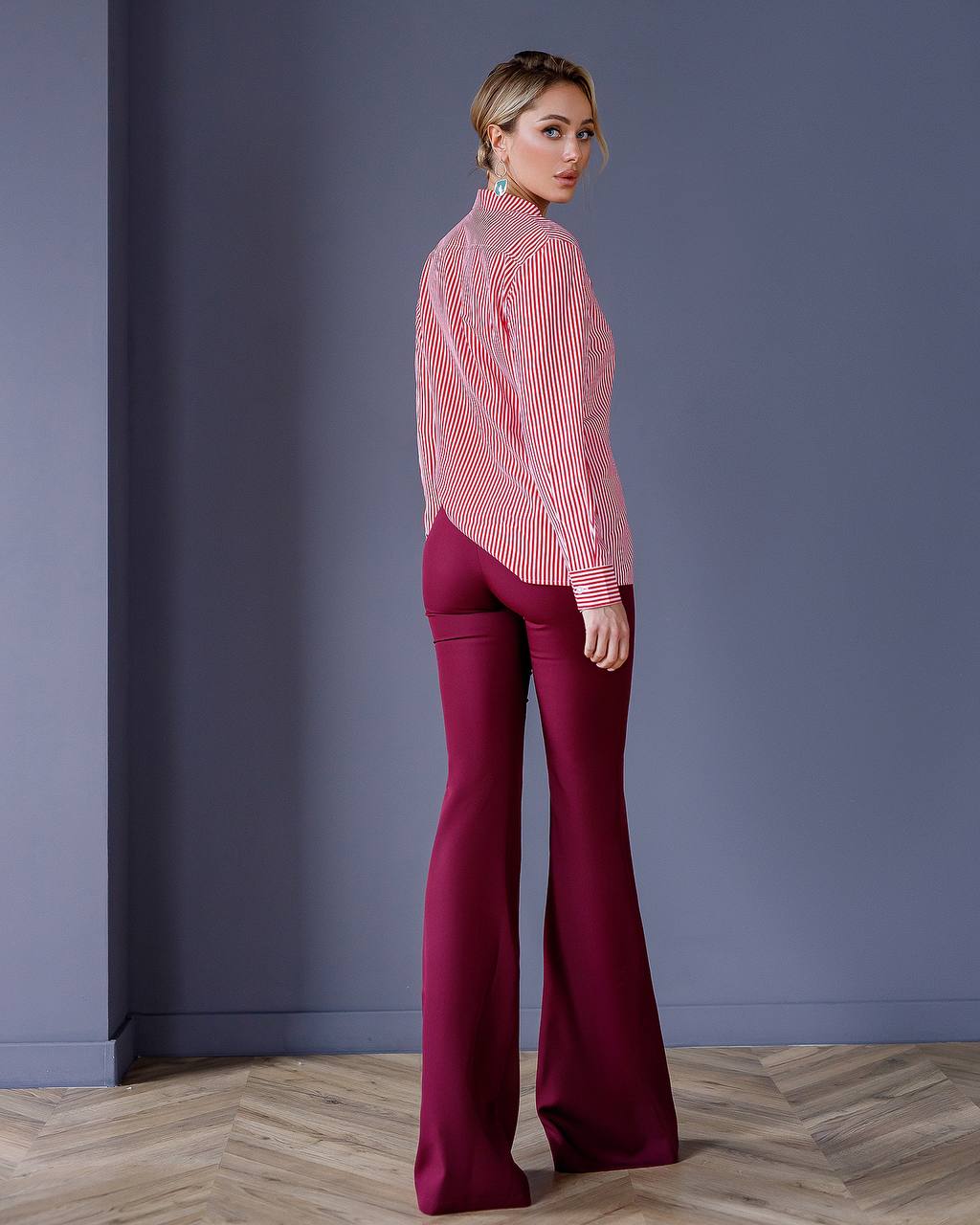 Woman wearing a red and white striped blouse and magenta pants against a gray wall.